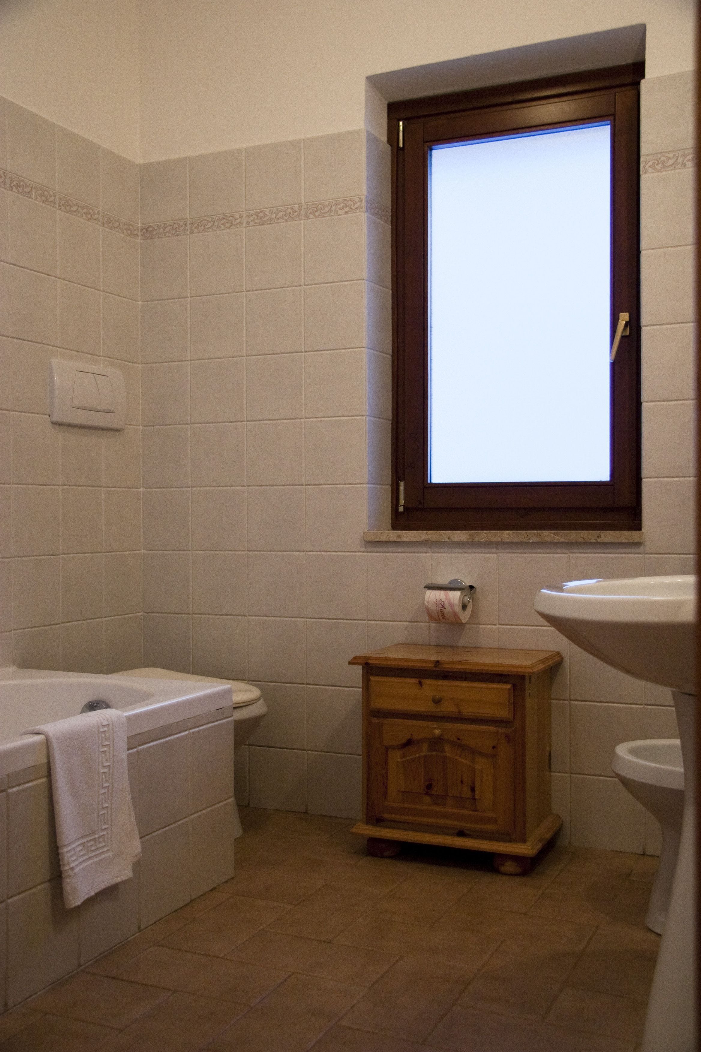 A bathroom with a bathtub, a wooden cabinet, a toilet, and a window.