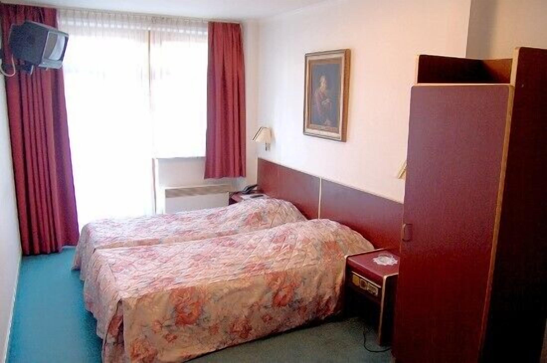 Ein Hotelzimmer mit zwei Betten, einem Schreibtisch, einem Fernseher und einem Kleiderschrank.