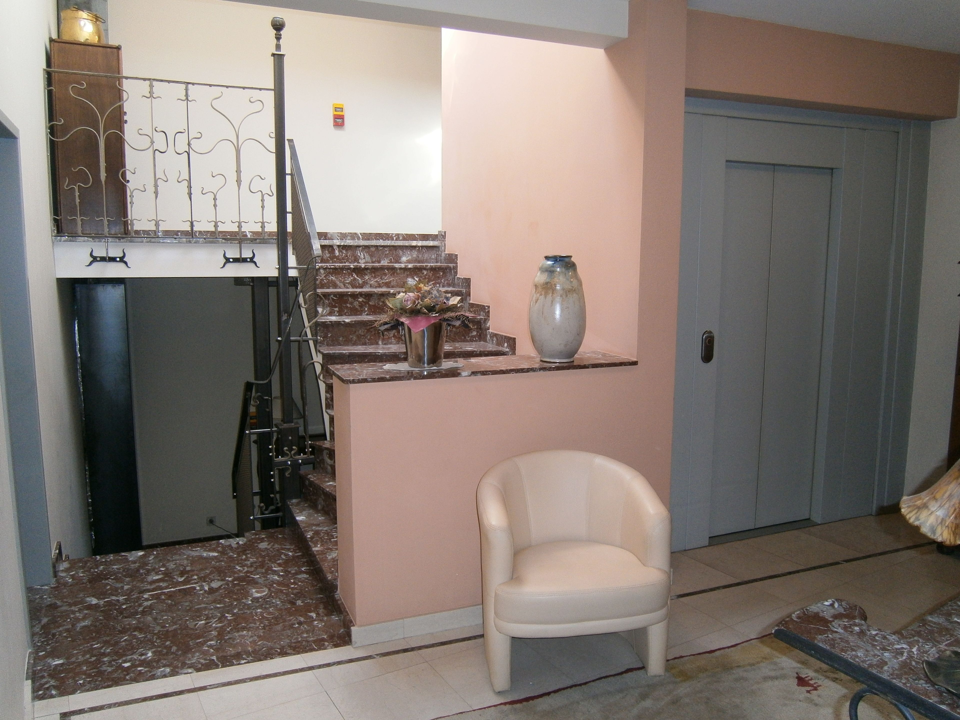 A living room with a marble staircase, a white chair, a vase, and a door.