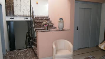 A living room with a marble staircase, a white chair, a vase, and a door.