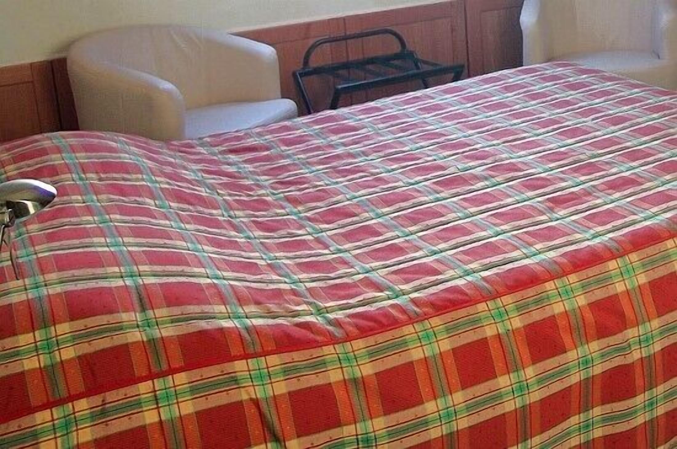 A bed with a plaid bedspread, a chair, and a metal chair rail.