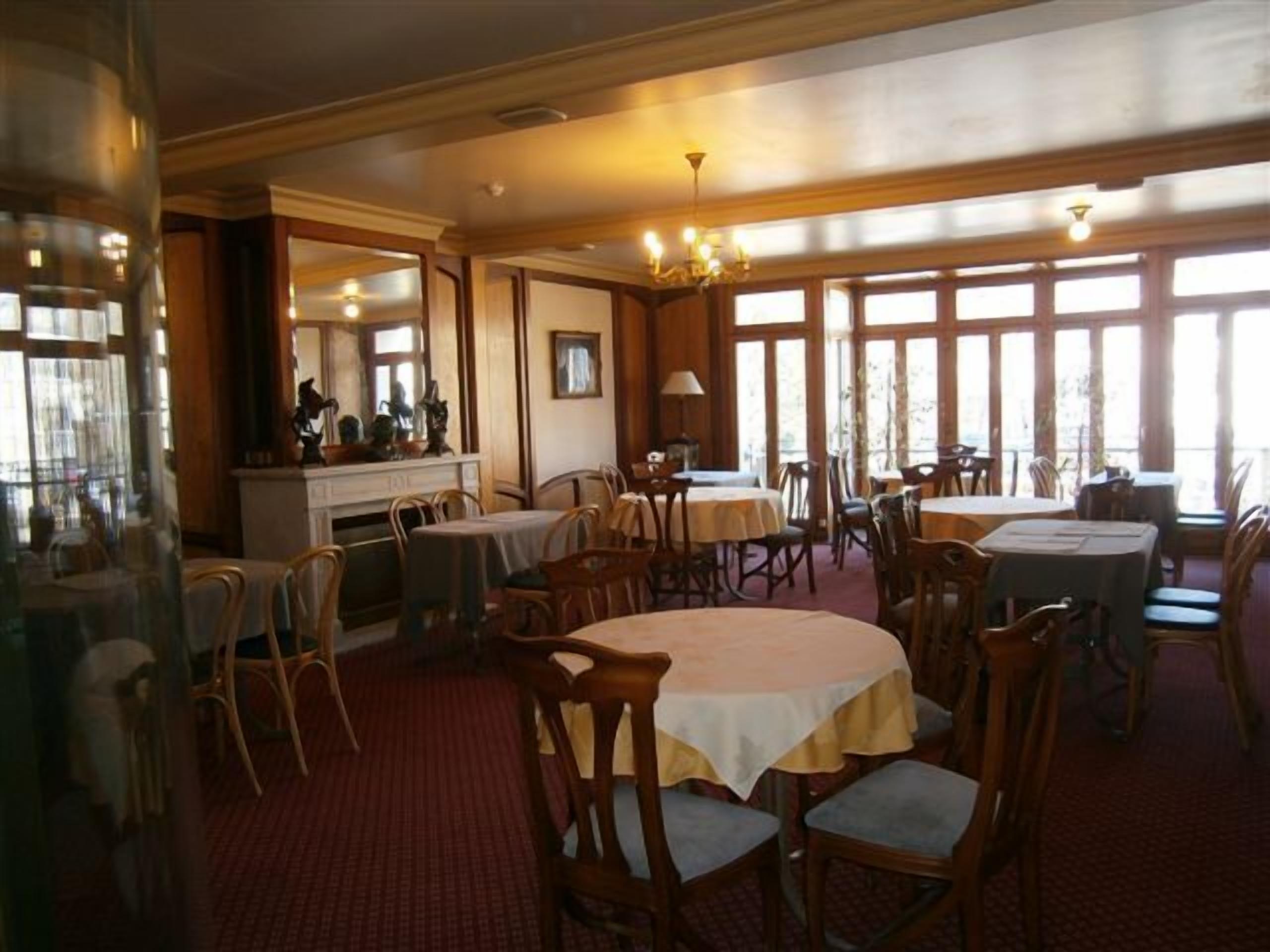 A dining area with multiple tables and chairs, large windows, and a chandelier.