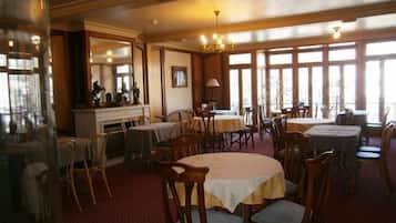 A dining area with multiple tables and chairs, large windows, and a chandelier.