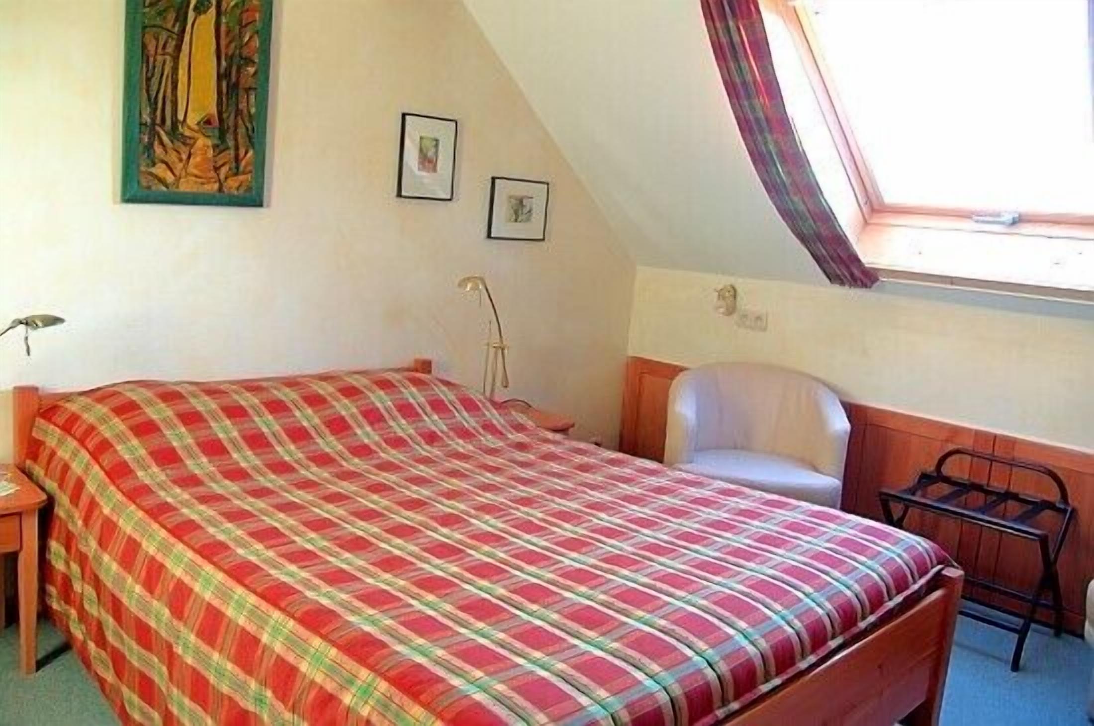 A bedroom with a bed, a chair, a desk, and a window.