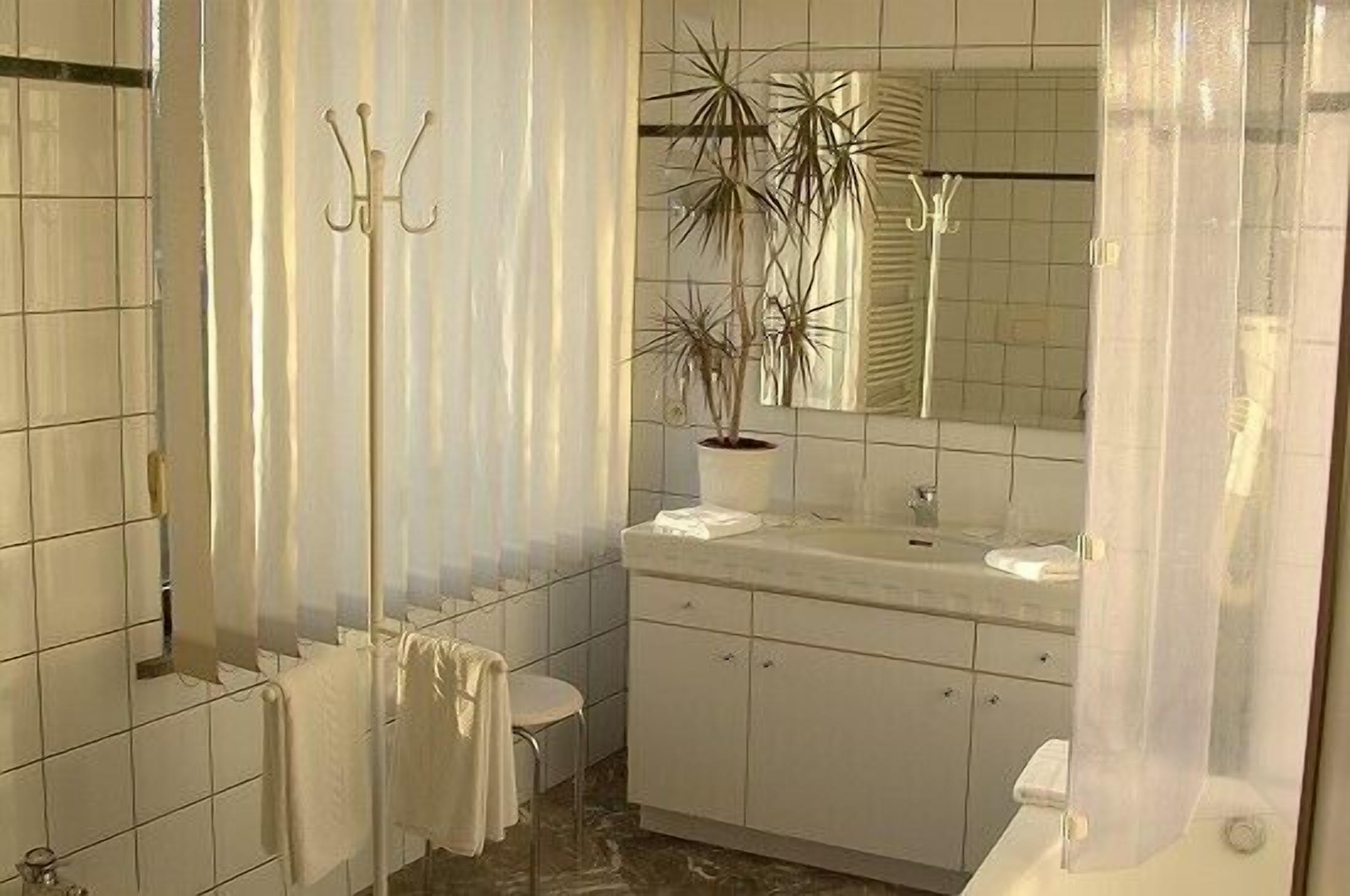 A bathroom with white tiles, a sink, a mirror, a toilet, and a shower curtain.