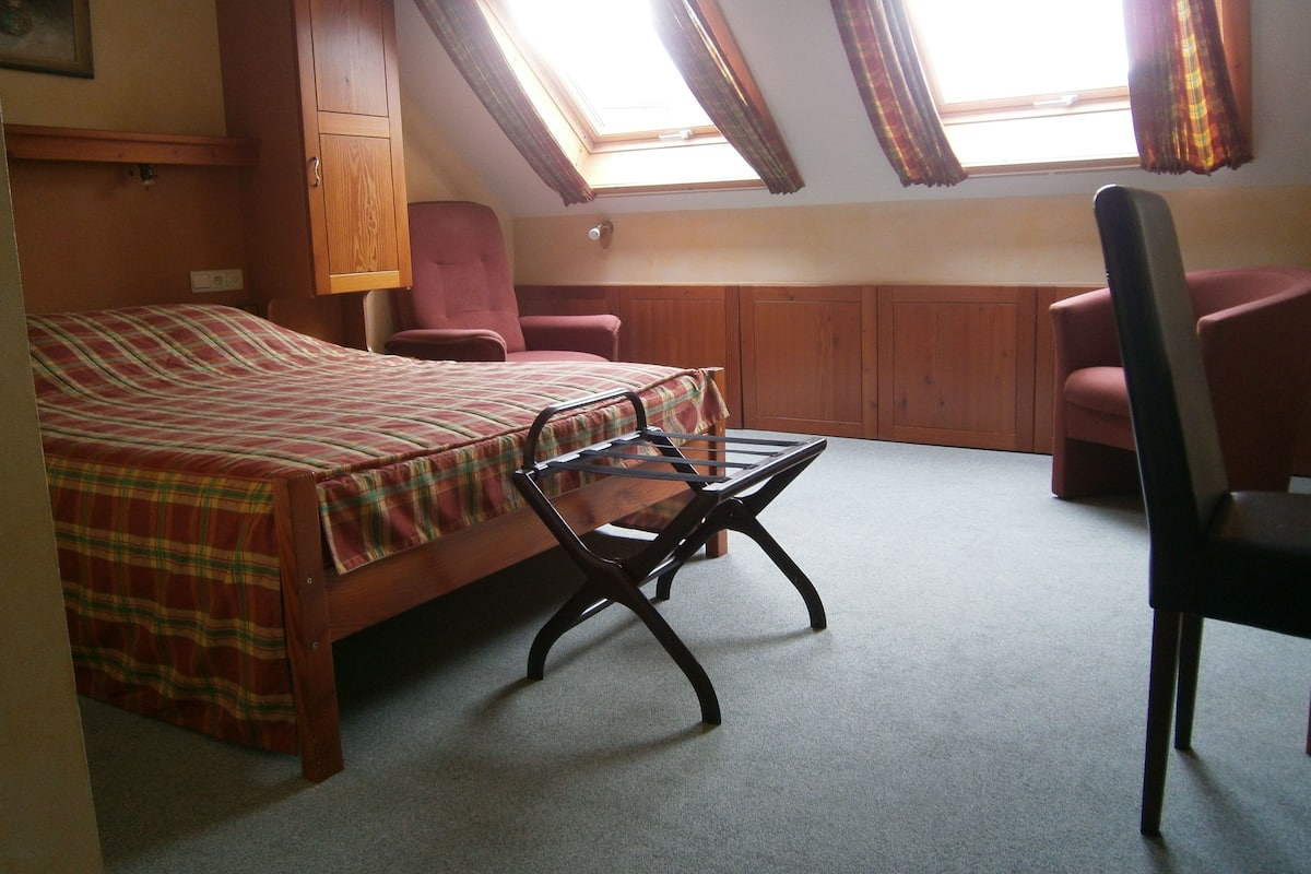 A bedroom with a bed, a chair, a desk, and a window with curtains.