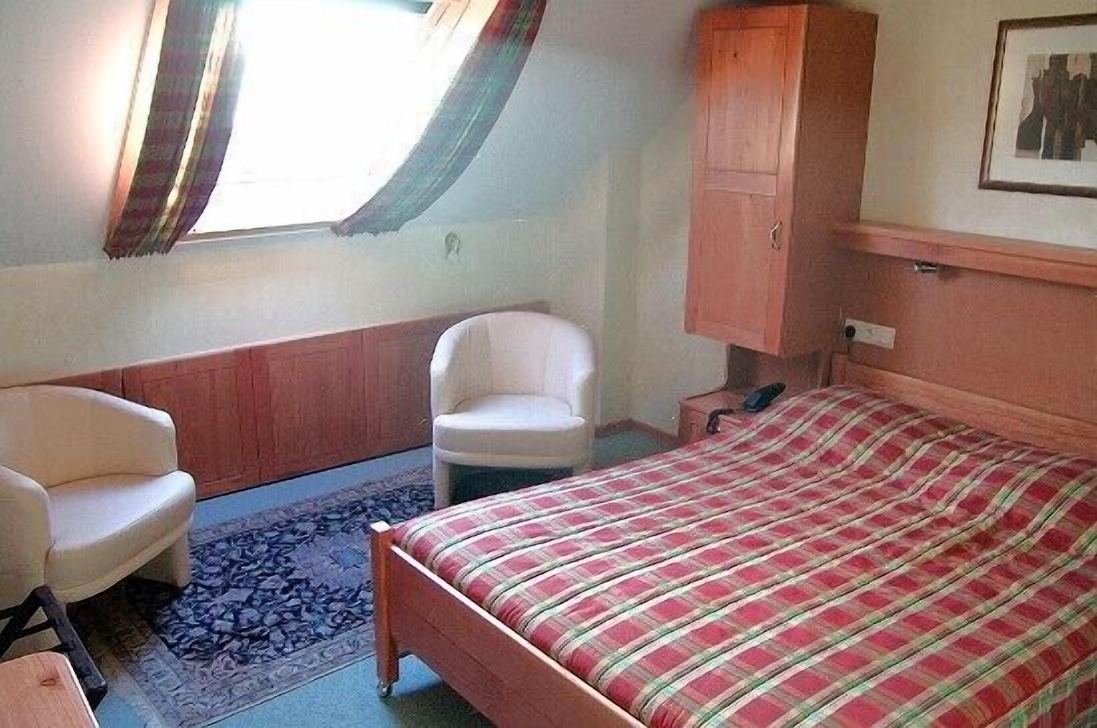 Un dormitorio con cama, una silla, un armario y una ventana con cortinas.
