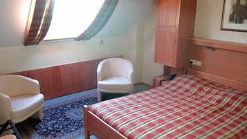Un dormitorio con cama, una silla, un armario y una ventana con cortinas.