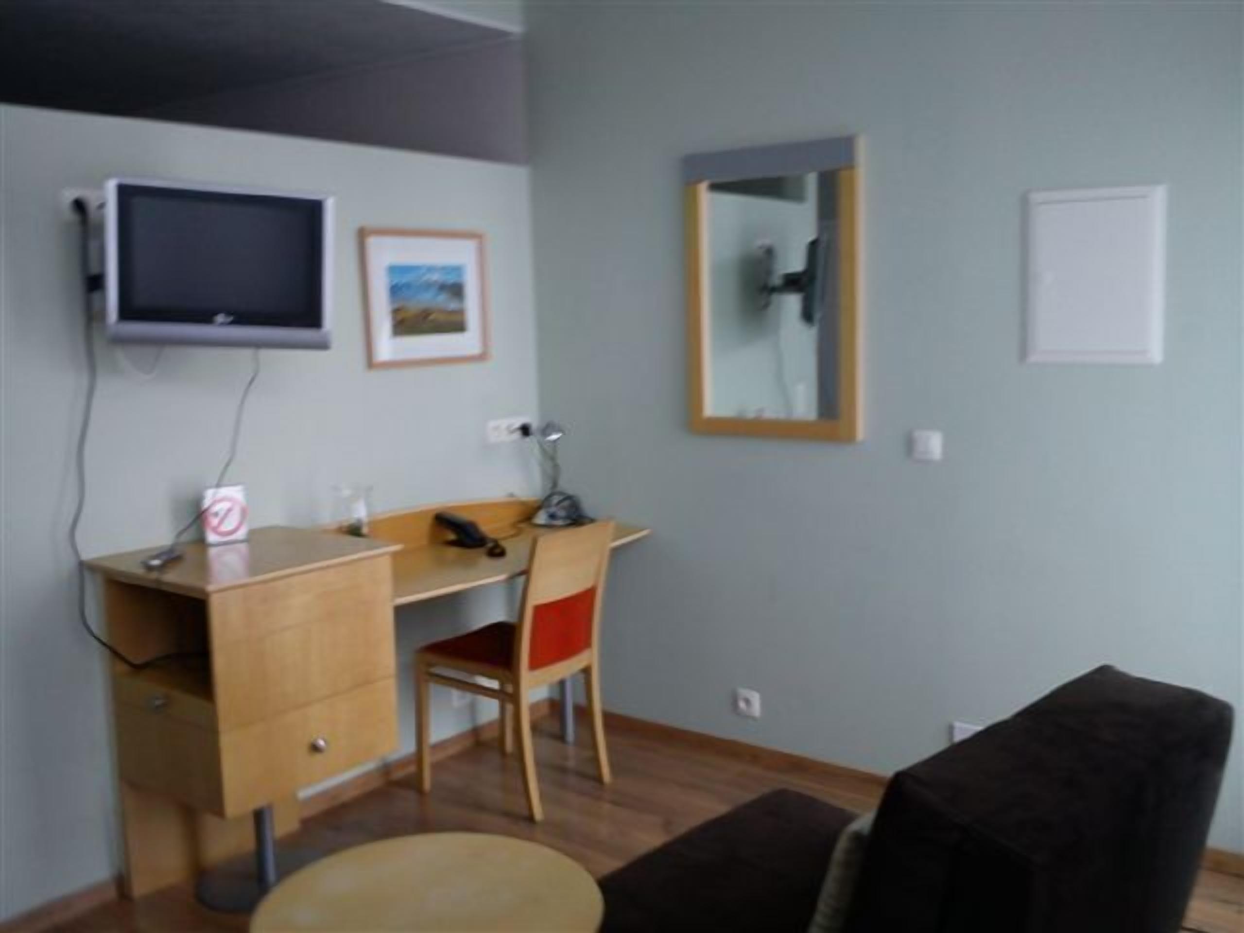 Une petite pièce simple, avec un bureau, une chaise et un téléviseur fixé au mur.