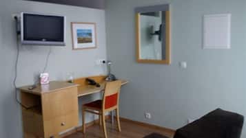 A small, simple room with a desk, chair, and a television mounted on the wall.