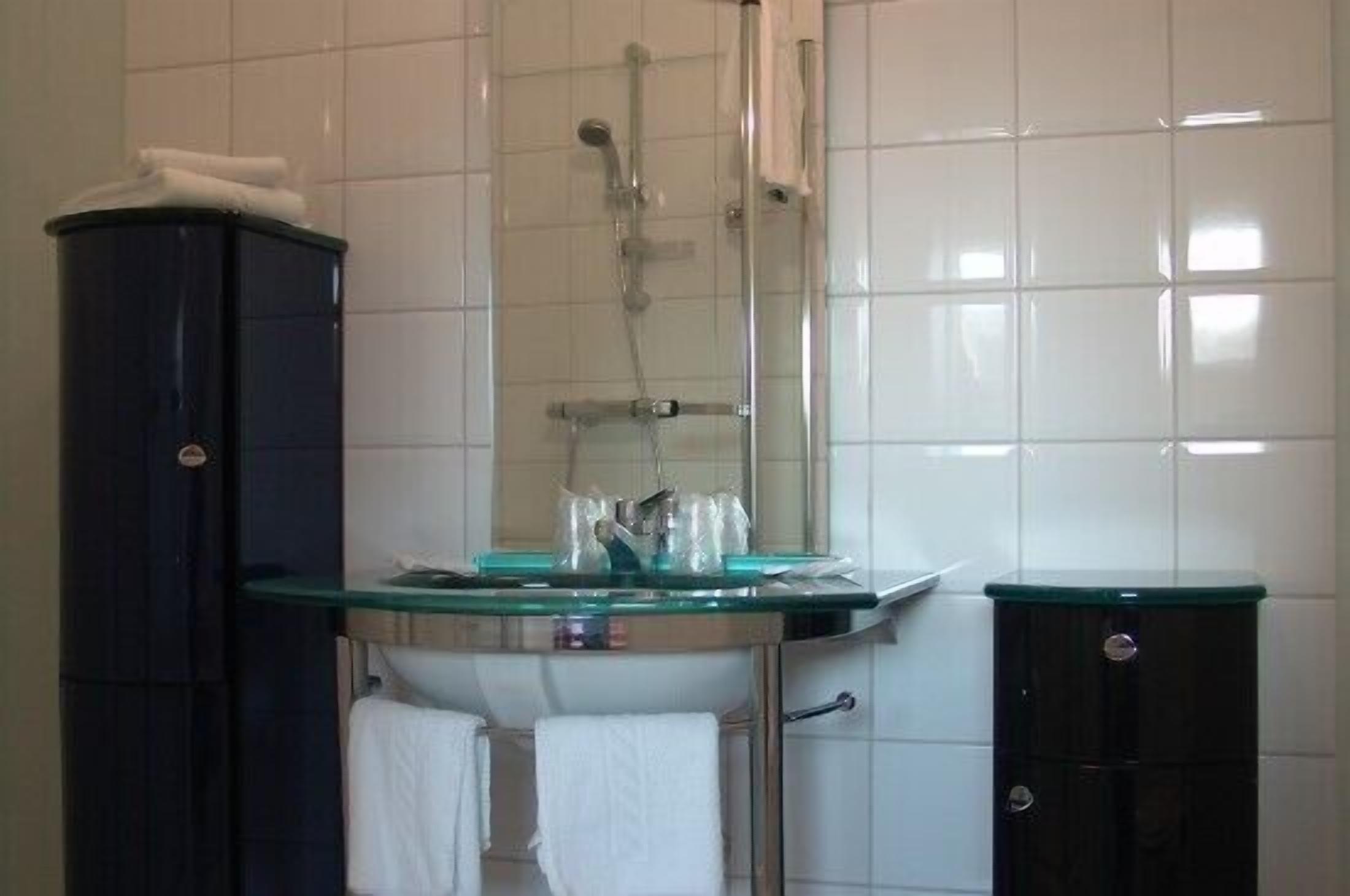 Ein Badezimmer mit Duschkabine aus Glas, einem schwarzen Schrank und einem Waschbecken aus Glas.