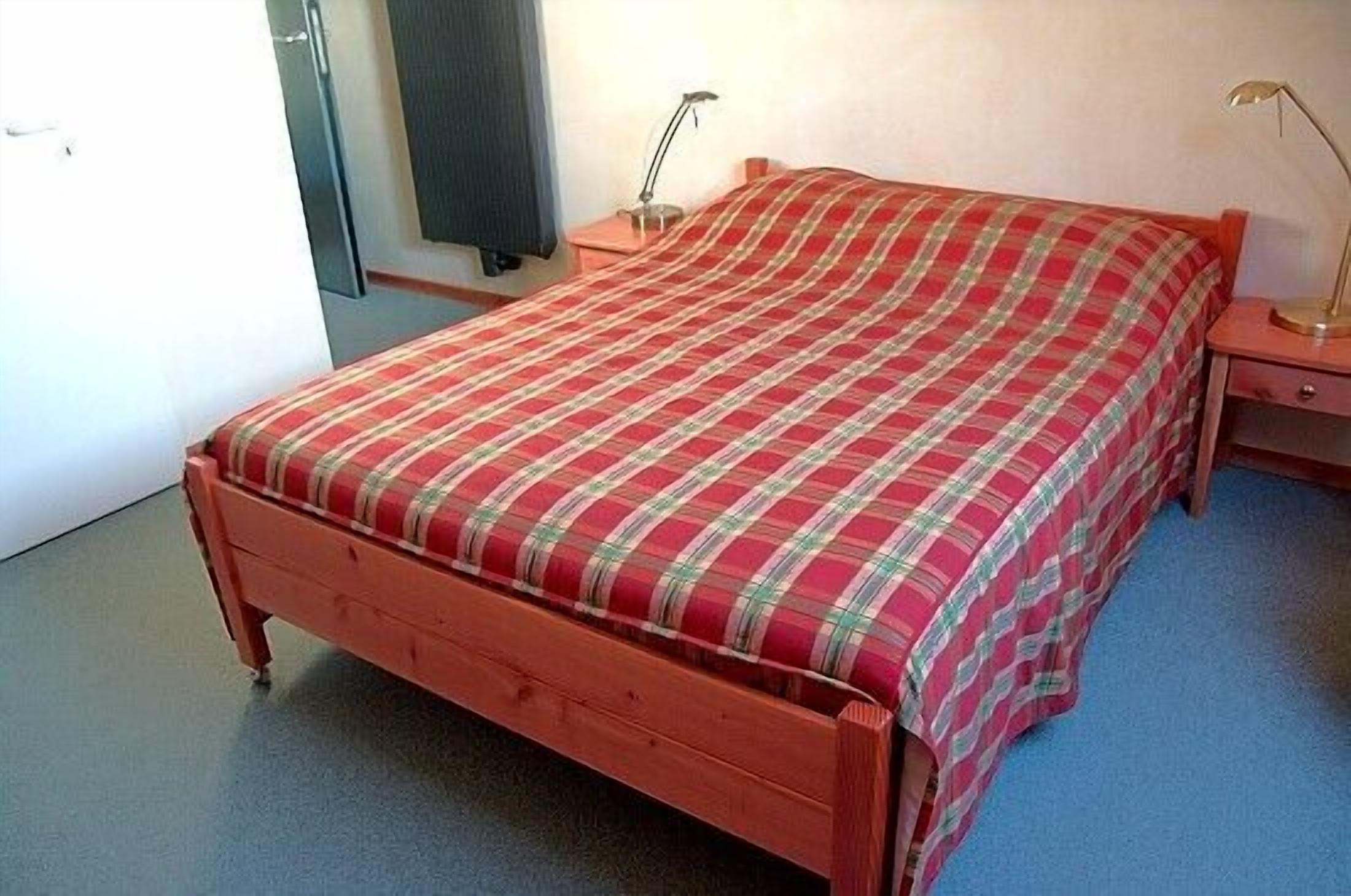 A single bed with a plaid bedspread in a room with a blue carpet.
