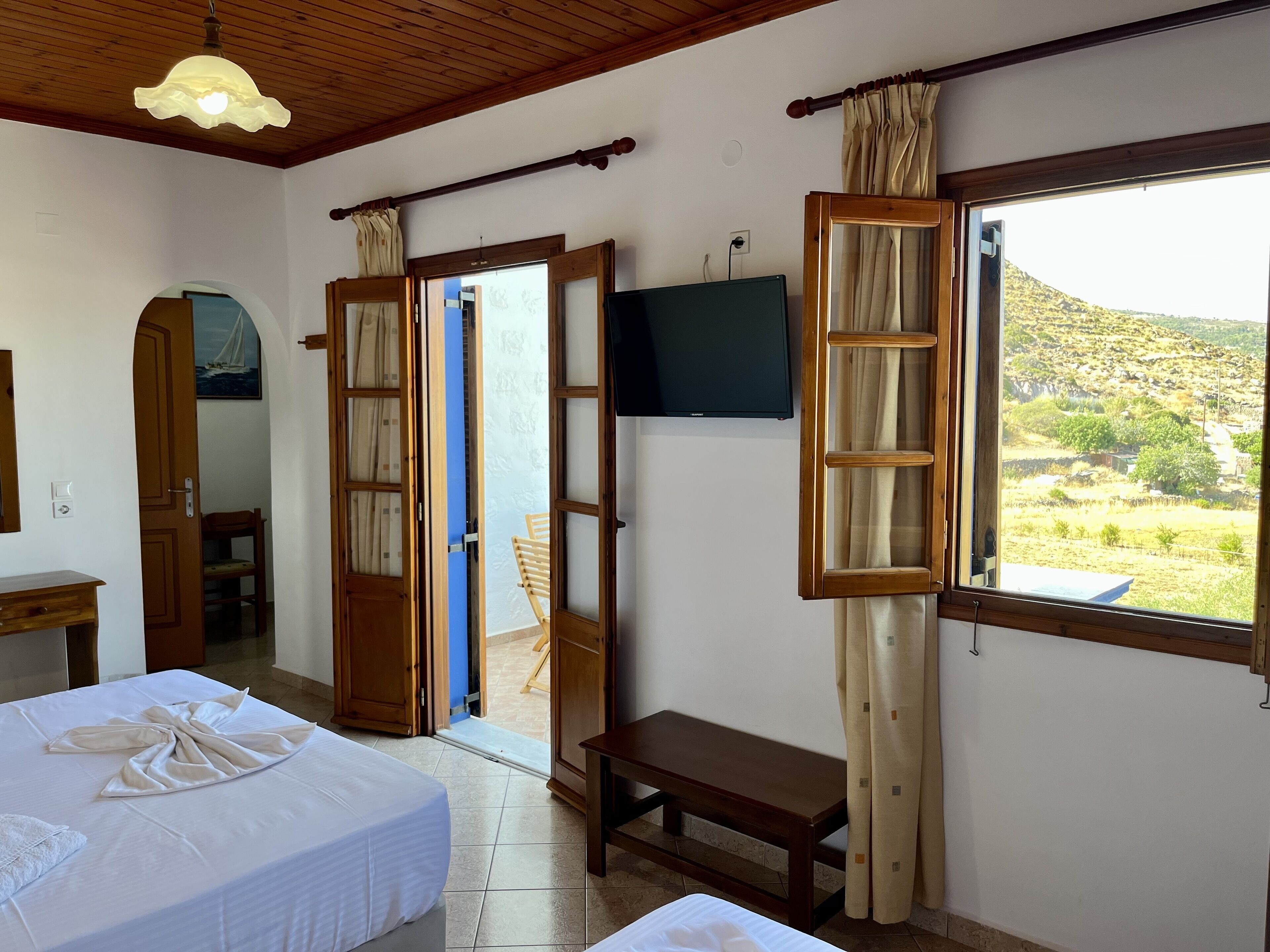 Una stanza con un letto, una panca, una televisione e vista su un paesaggio collinare attraverso una finestra.