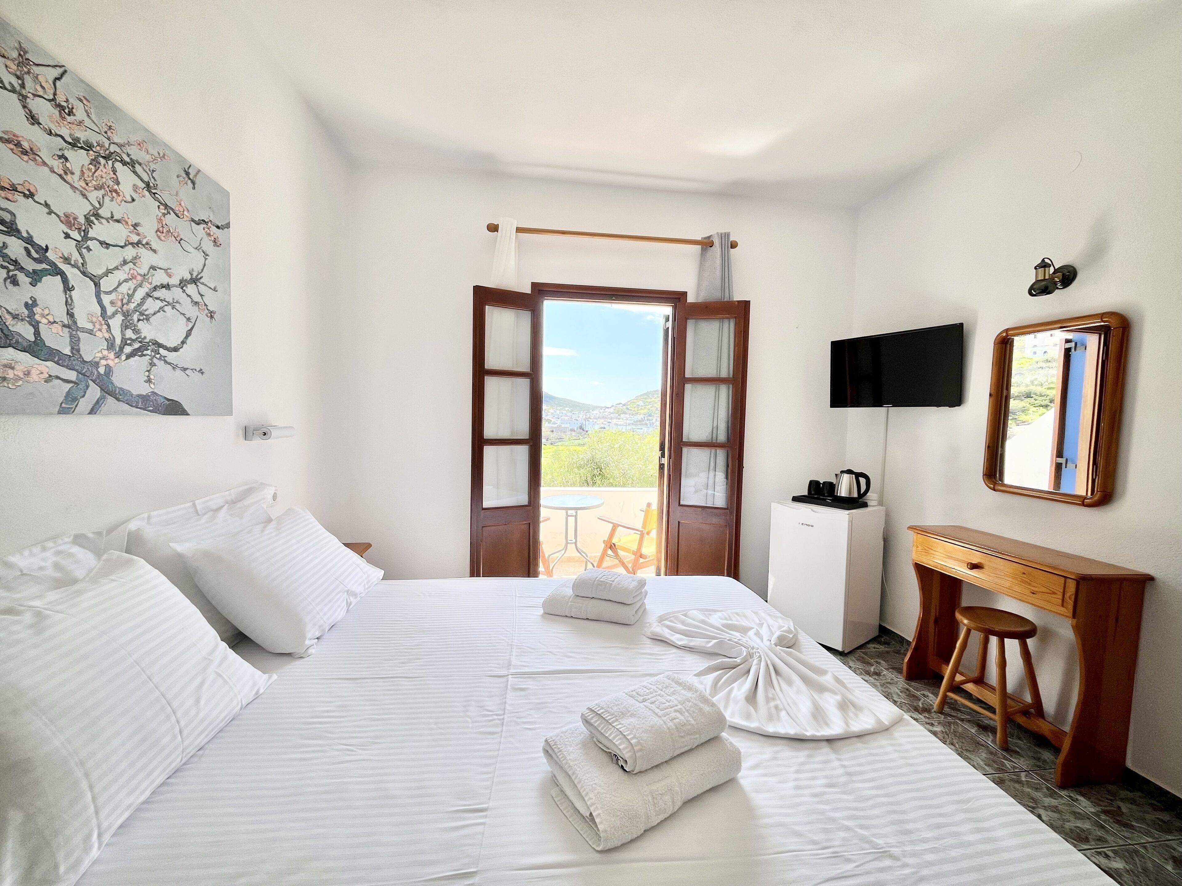 Habitación de hotel con cama, escritorio, silla, televisión y vistas al exterior.