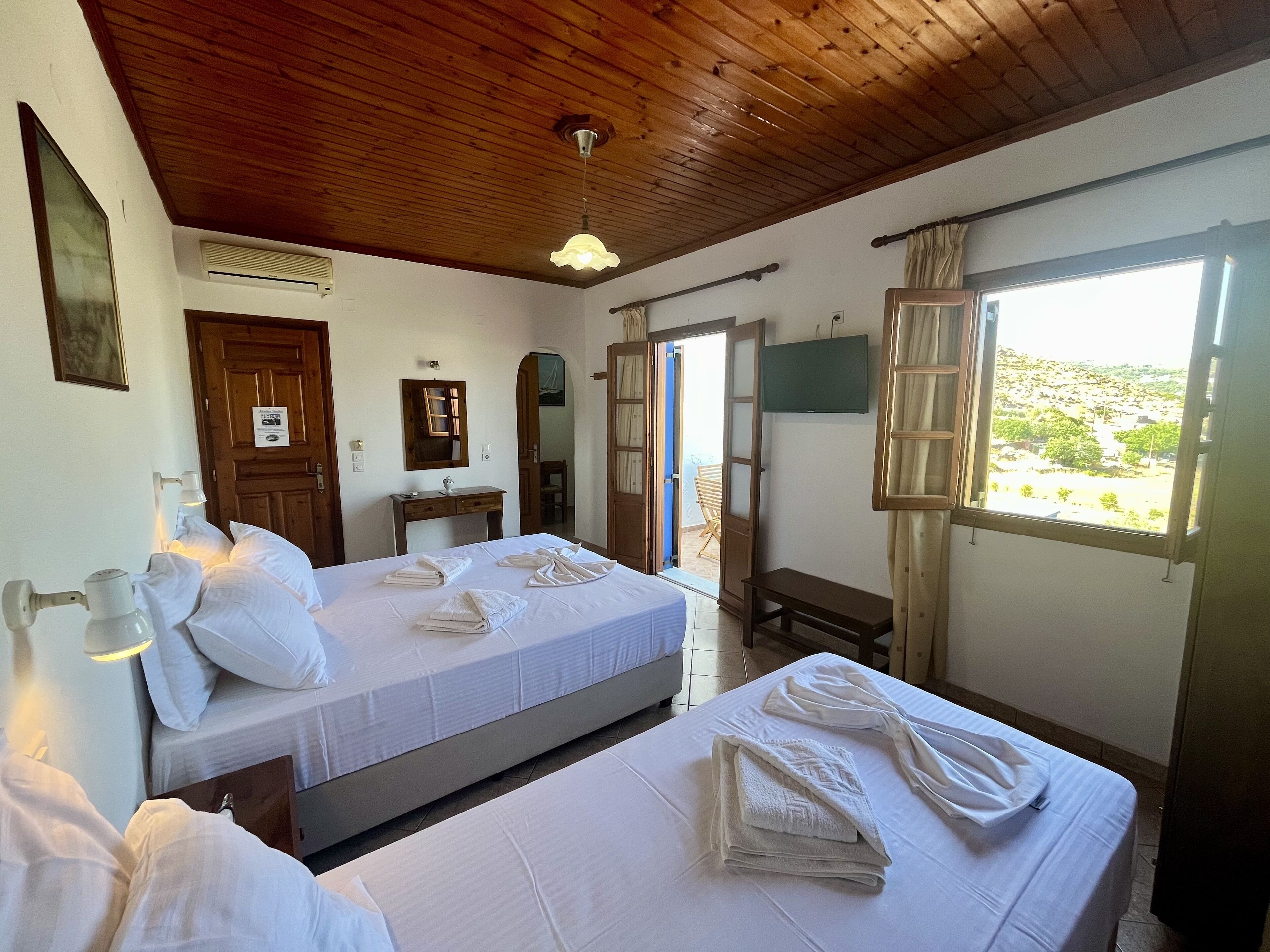 A hotel room with two beds, a wooden ceiling, a TV, and a window with a view.