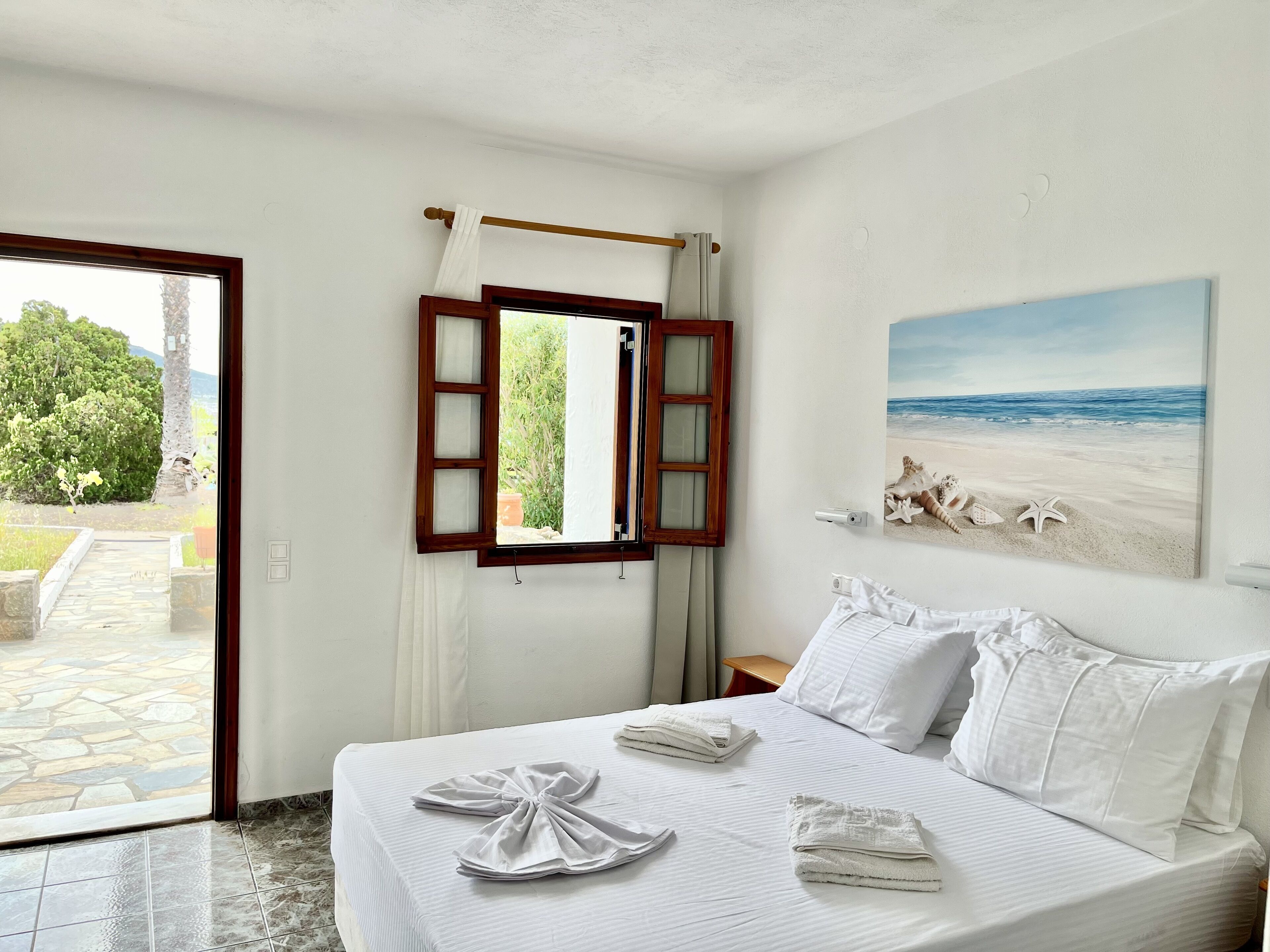 Ein Hotelzimmer mit einem Bett, einem Strandbild und Blick ins Freie.