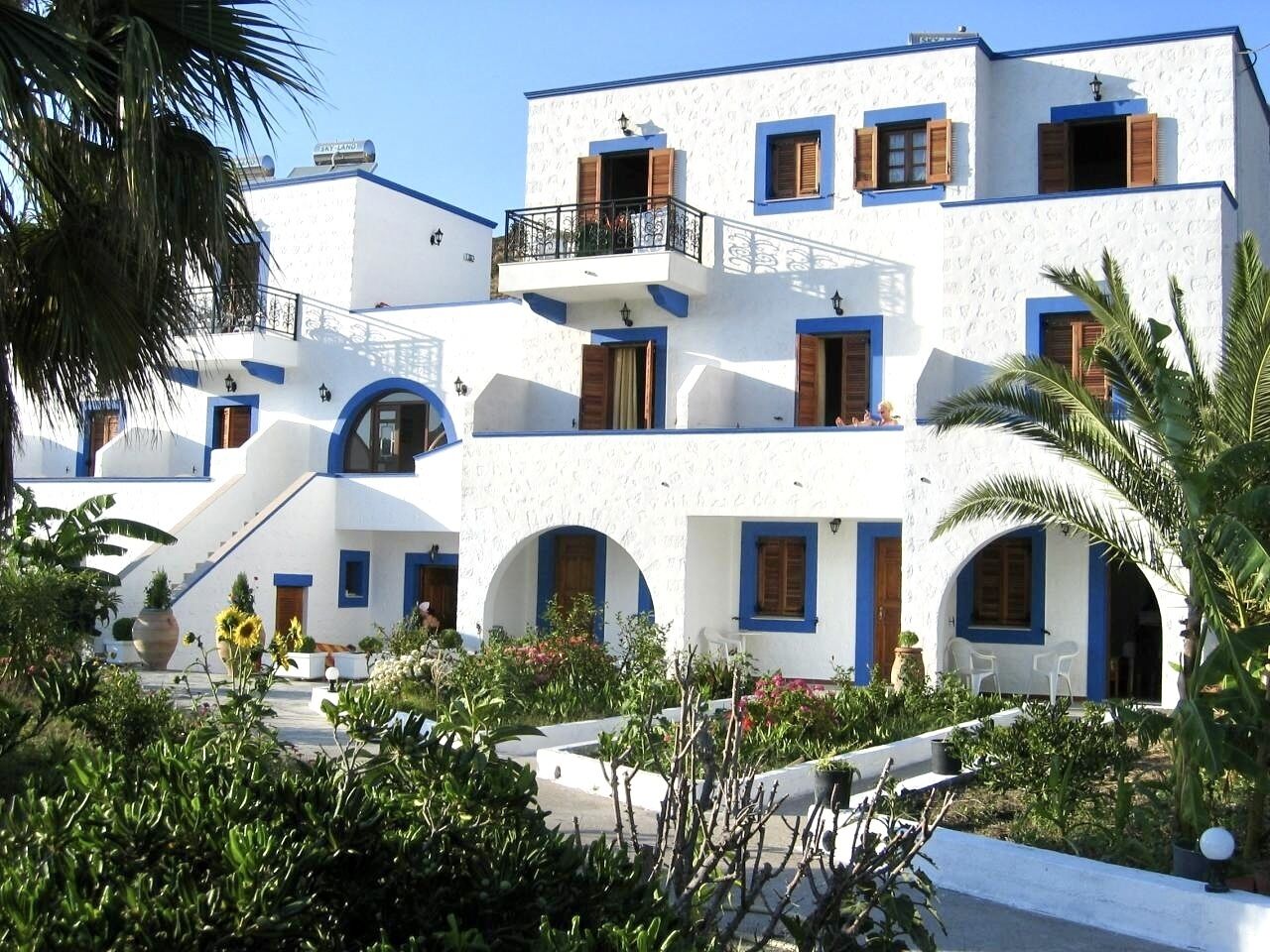 A white building with blue accents, multiple balconies, and arched doorways.