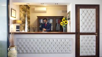 Un'area reception con un uomo dietro al bancone, un vaso con girasoli e un'ampia porta in legno con pannello imbottito bianco.