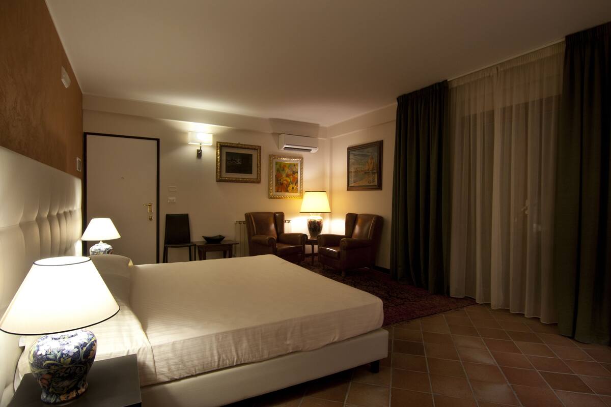 Een hotelkamer met een groot bed, twee stoelen, een tafel, een lamp en een schilderij aan de muur.