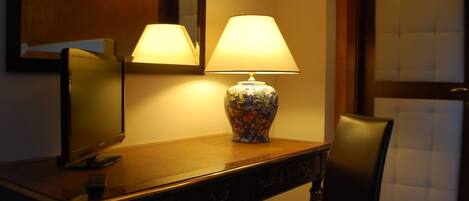 Una habitación de hotel con un escritorio de madera, televisor, lámpara y una silla.