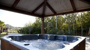 A hot tub under a wooden pergola with a view of trees and hills.