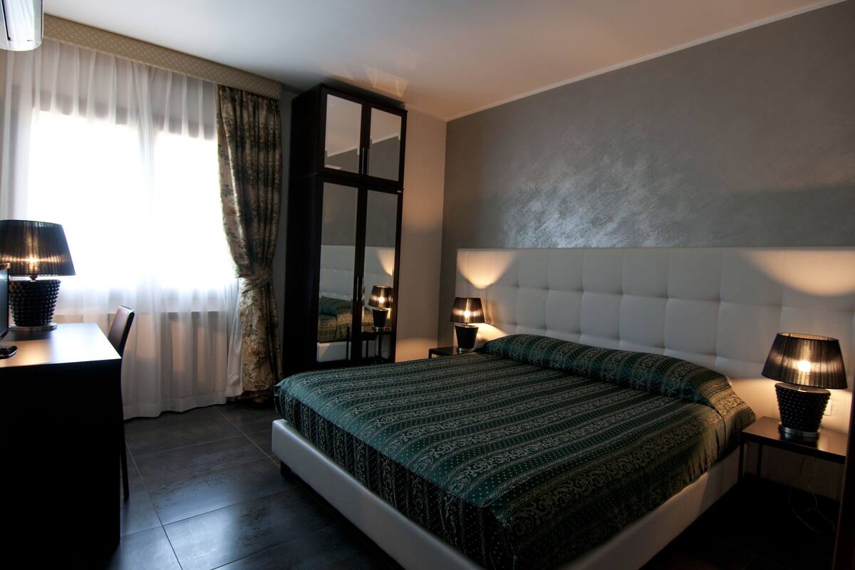 Een moderne slaapkamer met een groot bed, twee nachtkastjes met lampen, een bureau en een kledingkast.
