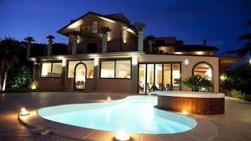 Enjoy a relaxing evening on the spacious balcony with a view, surrounded by lush potted plants and a serene swimming pool.