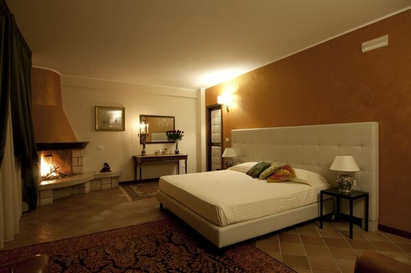 Una habitación de hotel con una cama grande, una chimenea, un escritorio y una mesita de noche.