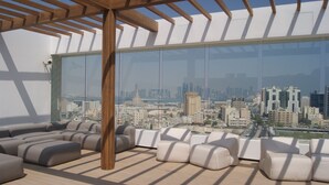 A modern rooftop lounge with a city view, featuring a wooden pergola, comfortable seating, and large glass windows. - K108 Hotel (Doha)