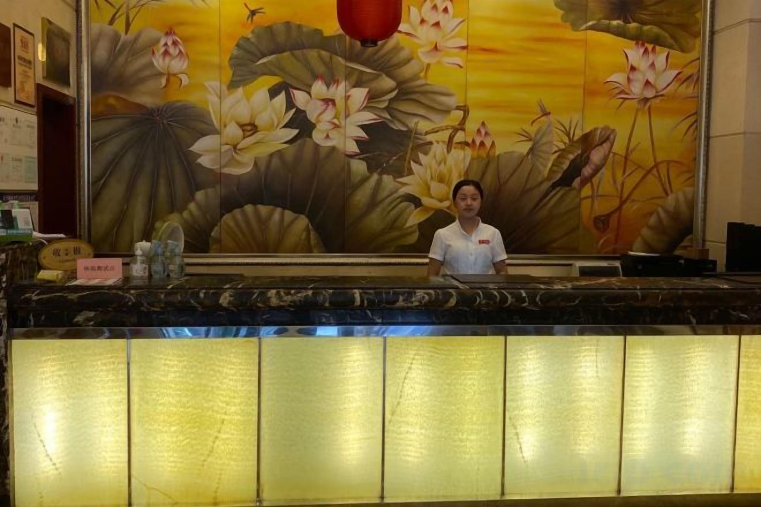 Un mostrador de recepción con una persona sentada detrás, un gran mural floral en la pared y una placa con el nombre.