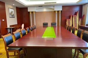 Een vergaderruimte met een lange tafel, stoelen en een groen tapijt.