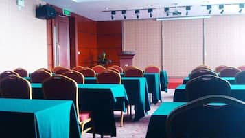A conference room with rows of tables and chairs, a podium, and a projector screen.