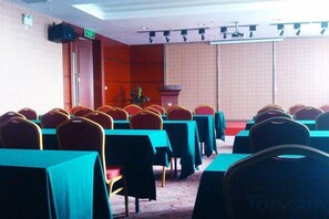 Un salón de conferencias con filas de mesas y sillas, un atril y una pantalla de proyector.