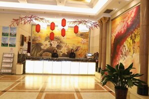 Un espace d’accueil d’hôtel comprenant un comptoir de réception, un grand tableau floral accroché au mur et une plante en pot.