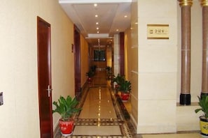 A hotel corridor with a carpeted floor, potted plants, and a sign on the wall. - Wenfeng City Hotel (Nantong)