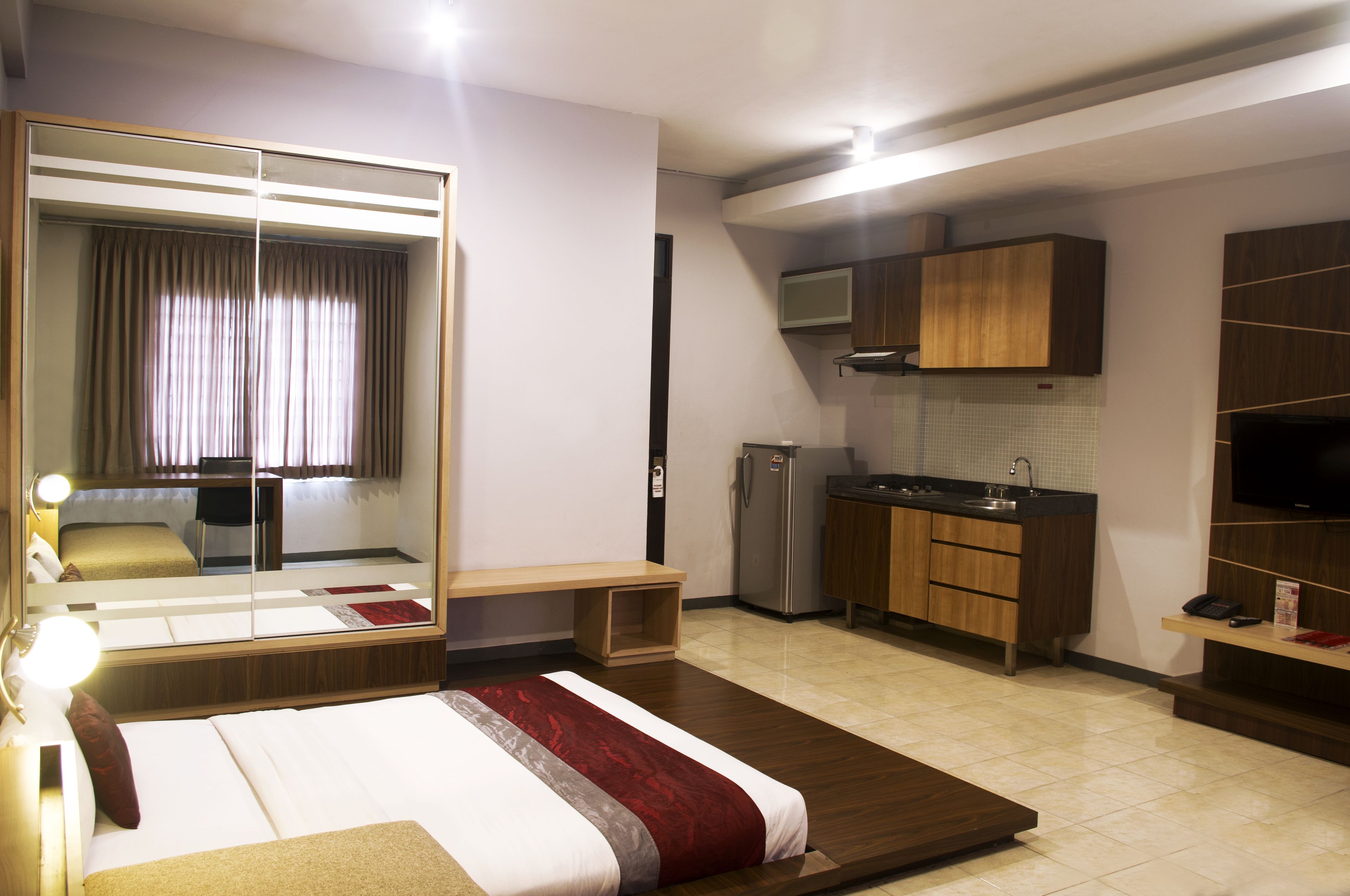 Une chambre d’hôtel équipée d’un lit, d’un miroir, d’un bureau, d’une chaise, d’une kitchenette et d’un téléviseur.