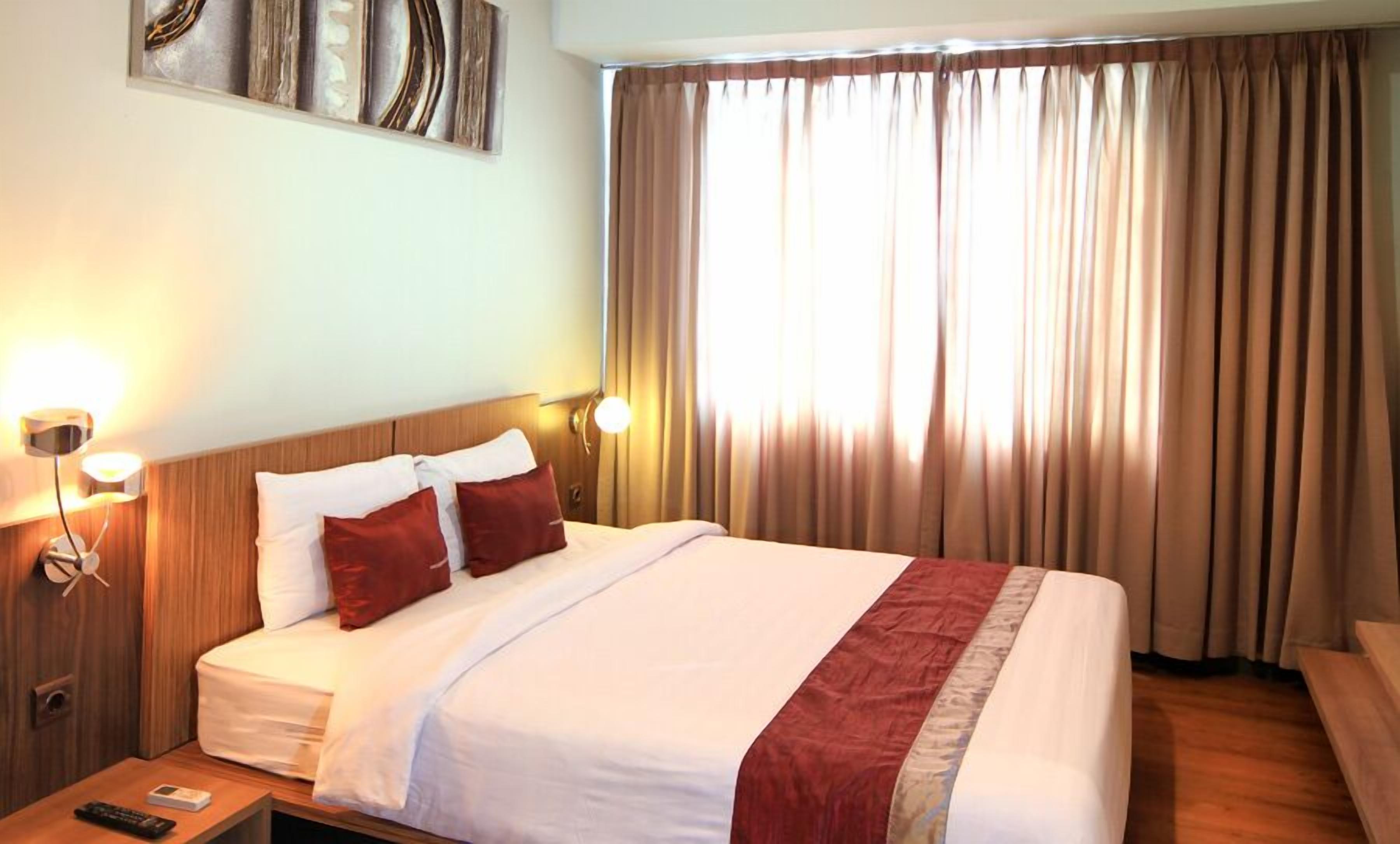 Habitación de hotel con una cama grande, dos lámparas de noche, cabecera de madera y vistas al exterior a través de cortinas.