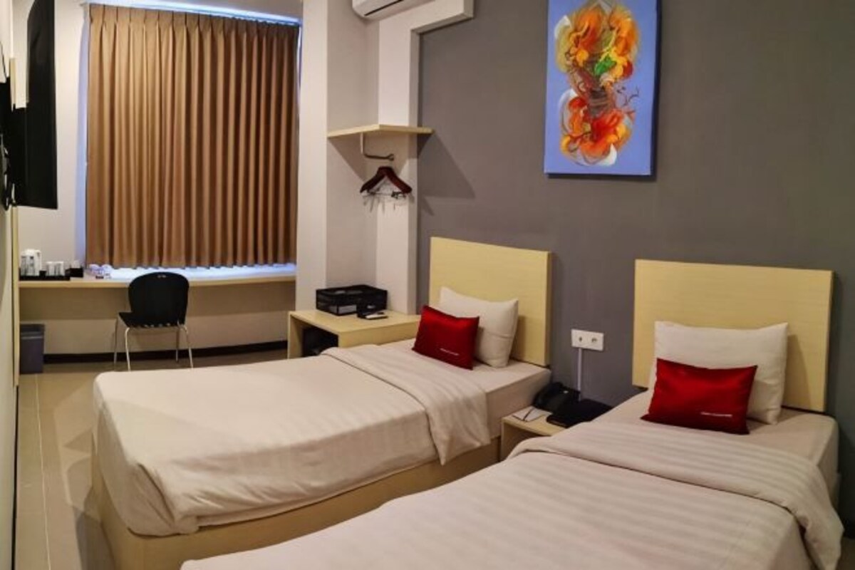A hotel room with two beds, a desk, a chair, a painting, and a window with curtains.