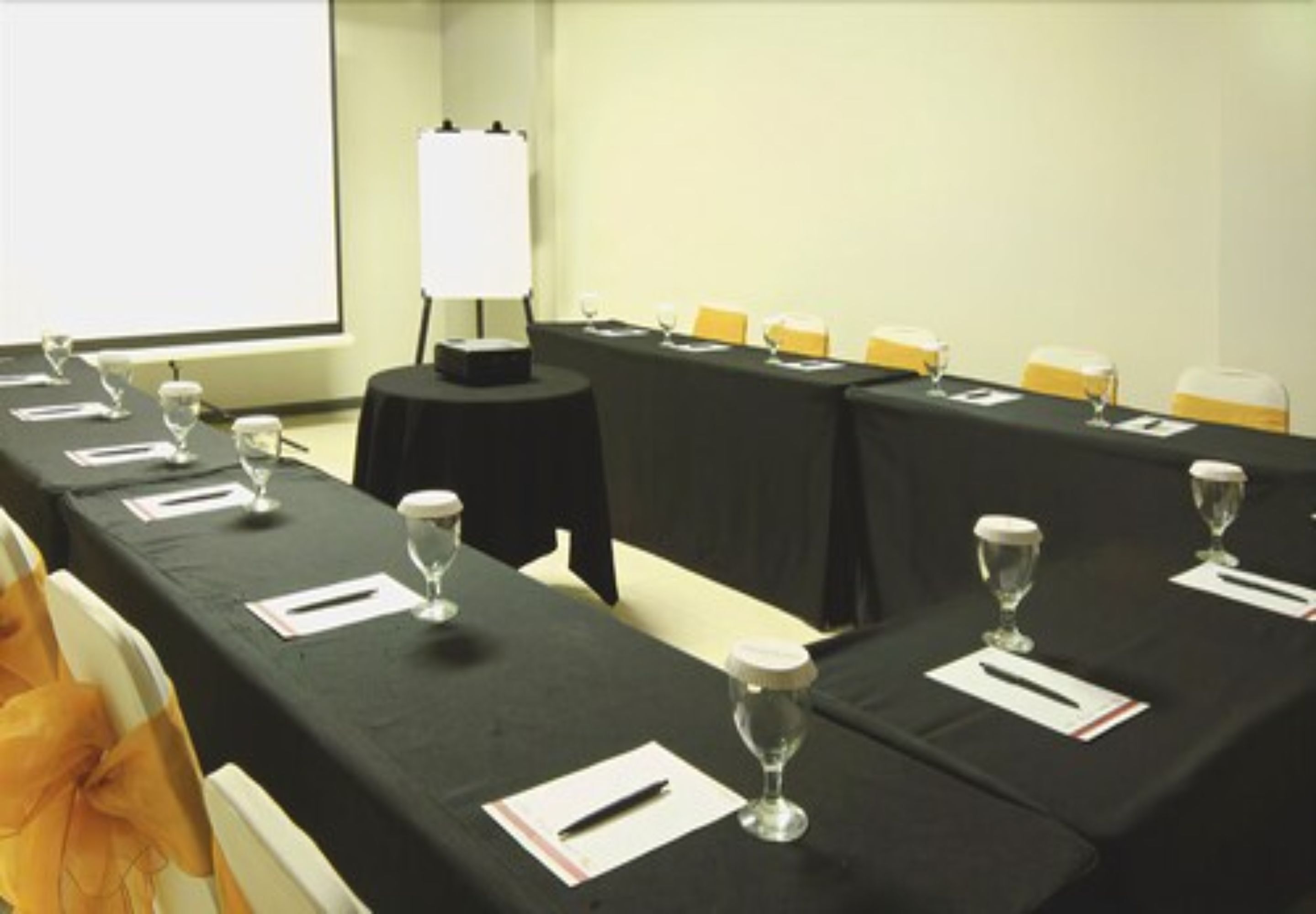 Une salle de conférence avec une longue table préparée pour une réunion, un écran de projection et un tableau blanc.