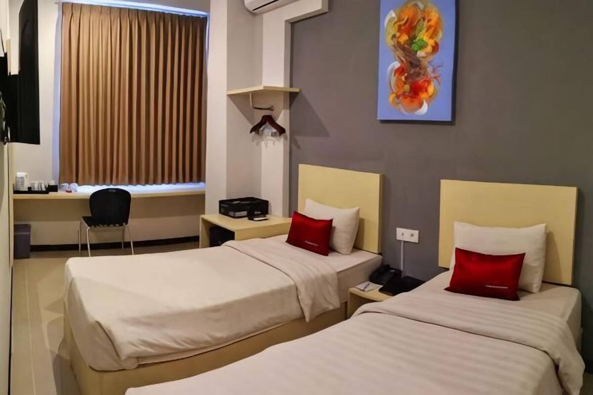 A hotel room with two beds, a desk, a chair, a painting, and a window with curtains.