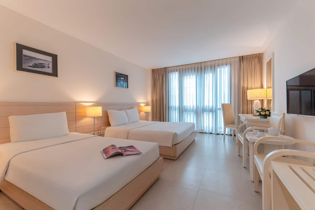 Habitación de hotel con dos camas, un escritorio con silla, un televisor y una ventana con cortinas.