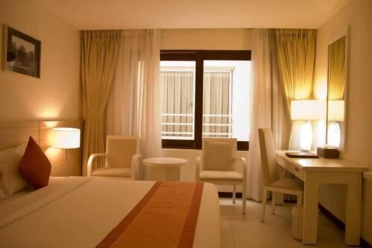 Una habitación de hotel con una cama, dos sillas, un escritorio, una lámpara y una ventana con cortinas.
