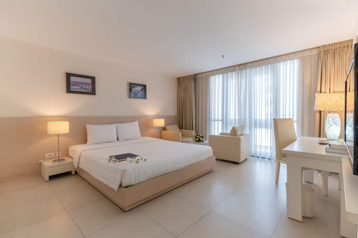 Habitación de hotel con una cama grande, dos mesitas de noche con lámparas, un escritorio, una silla y un ventanal con cortinas.