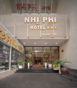 Exterior del hotel NHPI con fachada moderna, amplio acceso de vidrio y plantas de interior visibles.