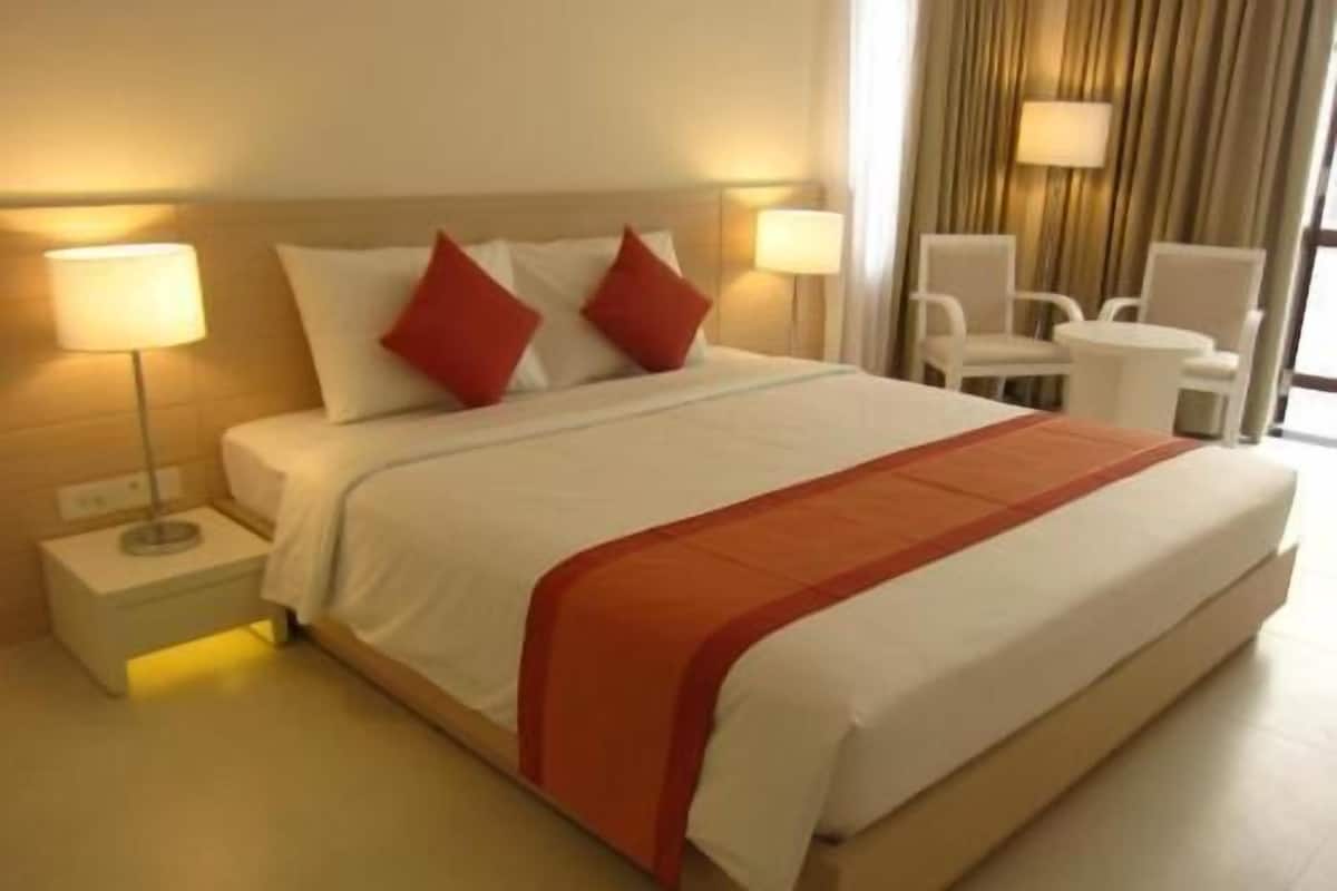 Una habitación de hotel con una cama grande, dos lámparas de noche, una silla y una mesita.