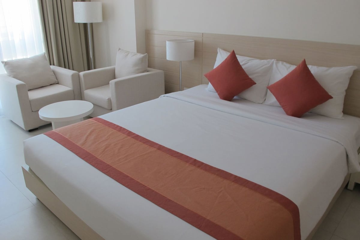 A hotel room with a large bed, two armchairs, a small round table, and two bedside lamps.