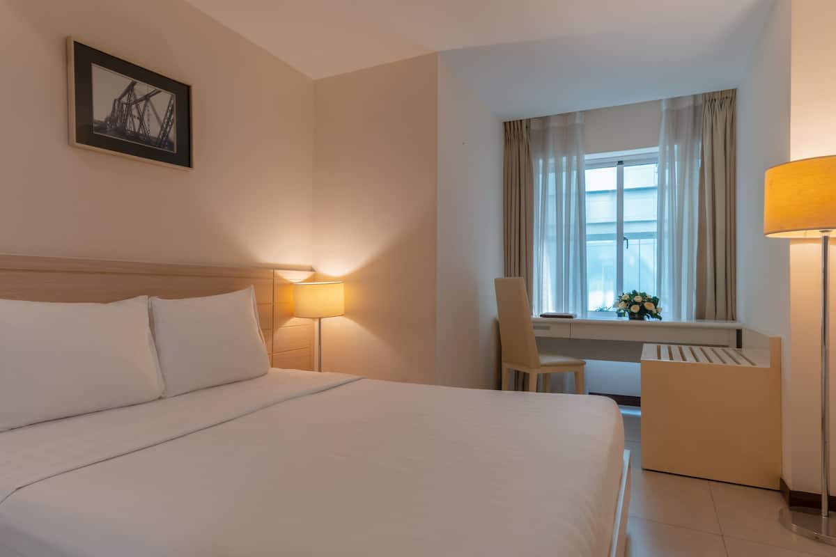 Habitación de hotel con una cama grande, lámparas de noche, un escritorio con silla y una ventana con cortinas.