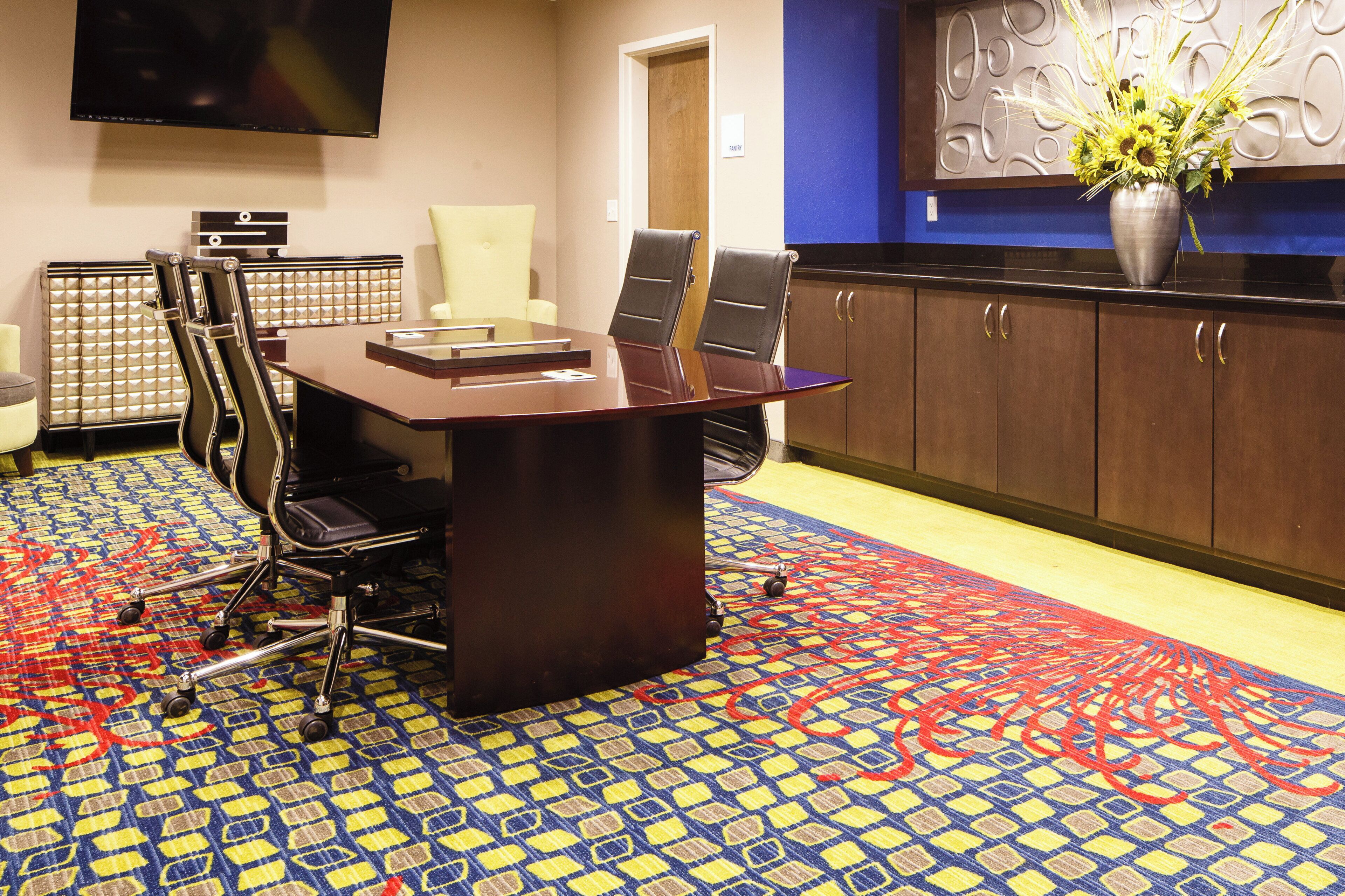 A conference room with a large table, chairs, a television, and a decorative wall piece.