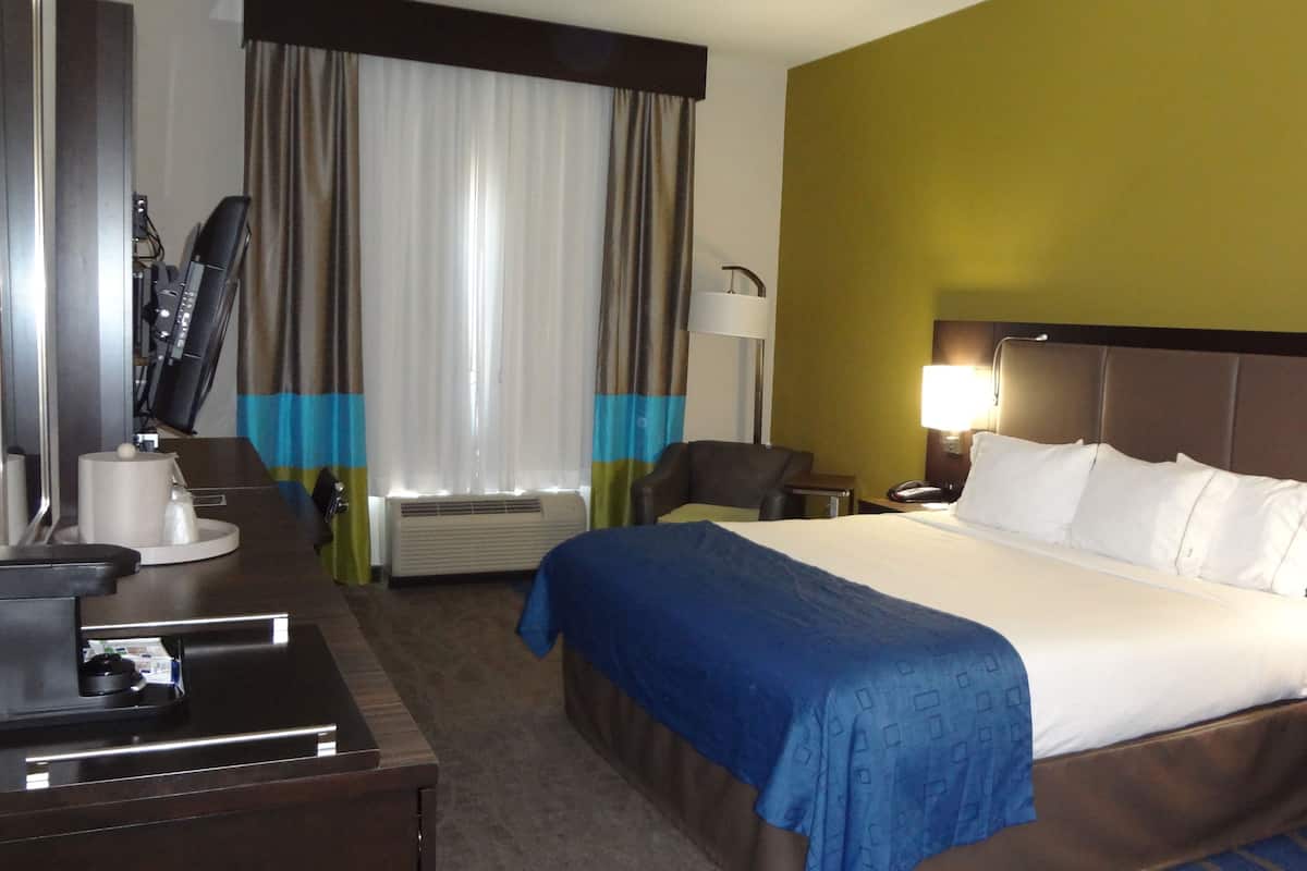 A hotel room with a bed, bedside tables, a desk, a chair, a desk lamp, a telephone, and a window with curtains.