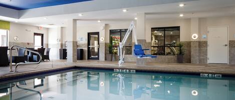An indoor swimming pool with a lifeguard stand, lounge chairs, and a clear poolside area.